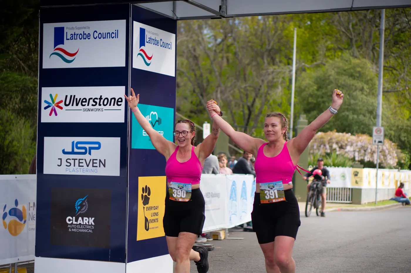 Two runners holding hands with arms raised as they reach the finish arch