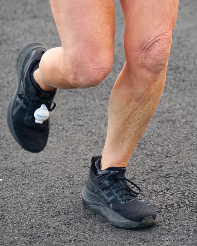 Close-up of a runner’s legs and black trail shoes mid-stride on asphalt